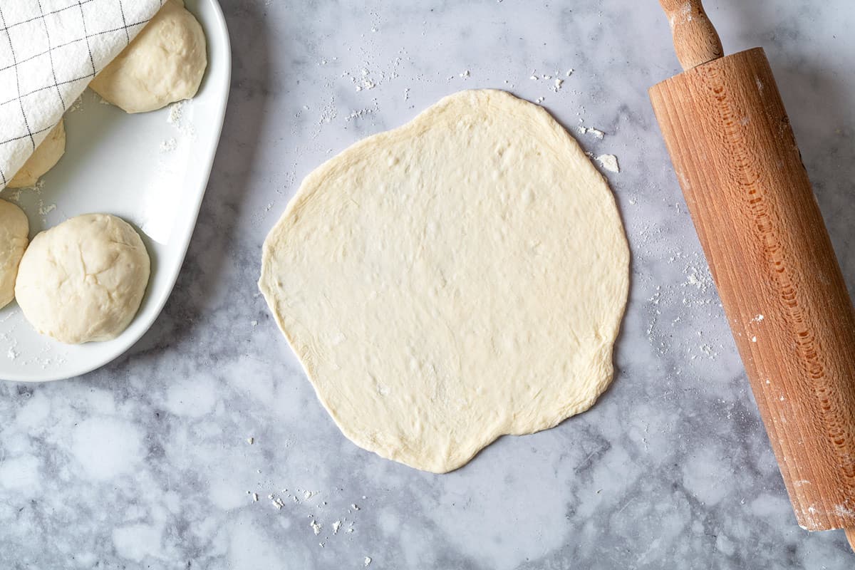 Lavash bread that has been rolled on a marble countertop with a wooden rolling pin. Everything has been dusted with flour to prevent sticking.