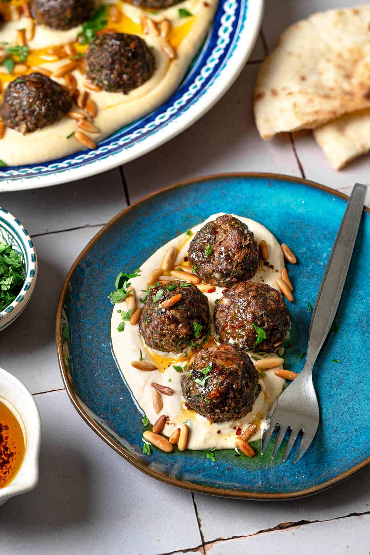 a close up of a serving of meatballs over hummus on a blue plate with a fork.