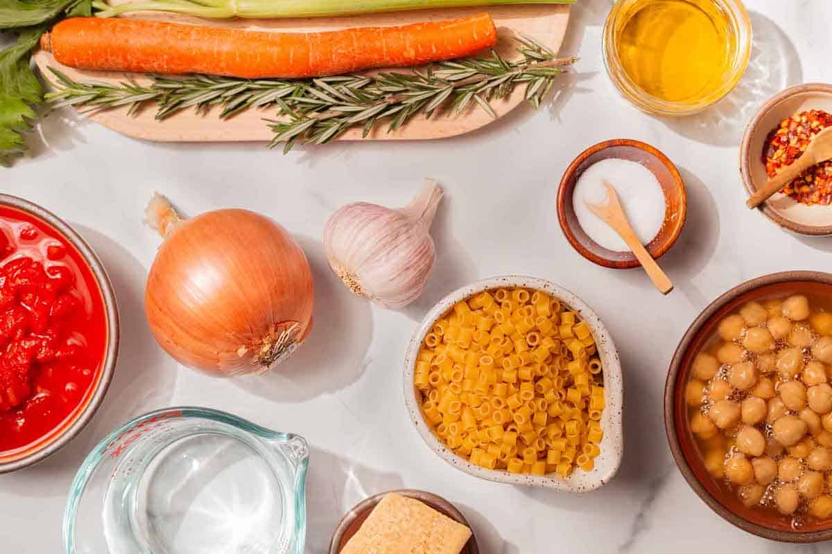 Ingredients for pasta e ceci, including pasta, salt, red pepper flakes, olive oil, carrots, tomato, rosemary, celery, chickpeas, onion, garlic, and parmesan.