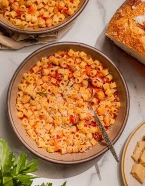 Overhead shot of a bowl of pasta e ceci with freshly grated parmesan cheese on top and parsley, parmesan, and bread on the side.