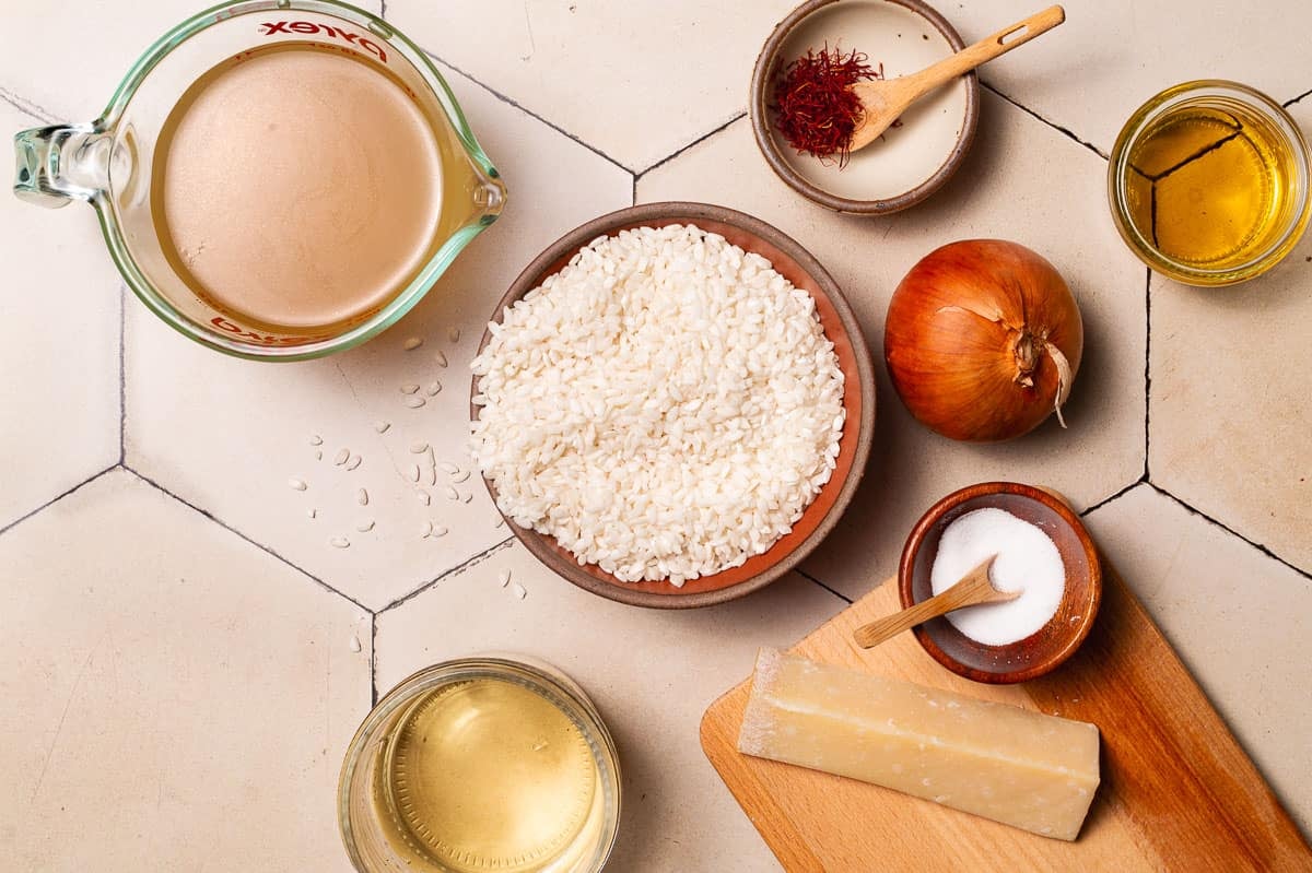 ingredients for risotto alla milanese saffron risotto including chicken broth, saffron threads, olive oil, onion, arborio rice, salt, white wine, and parmesan cheese.