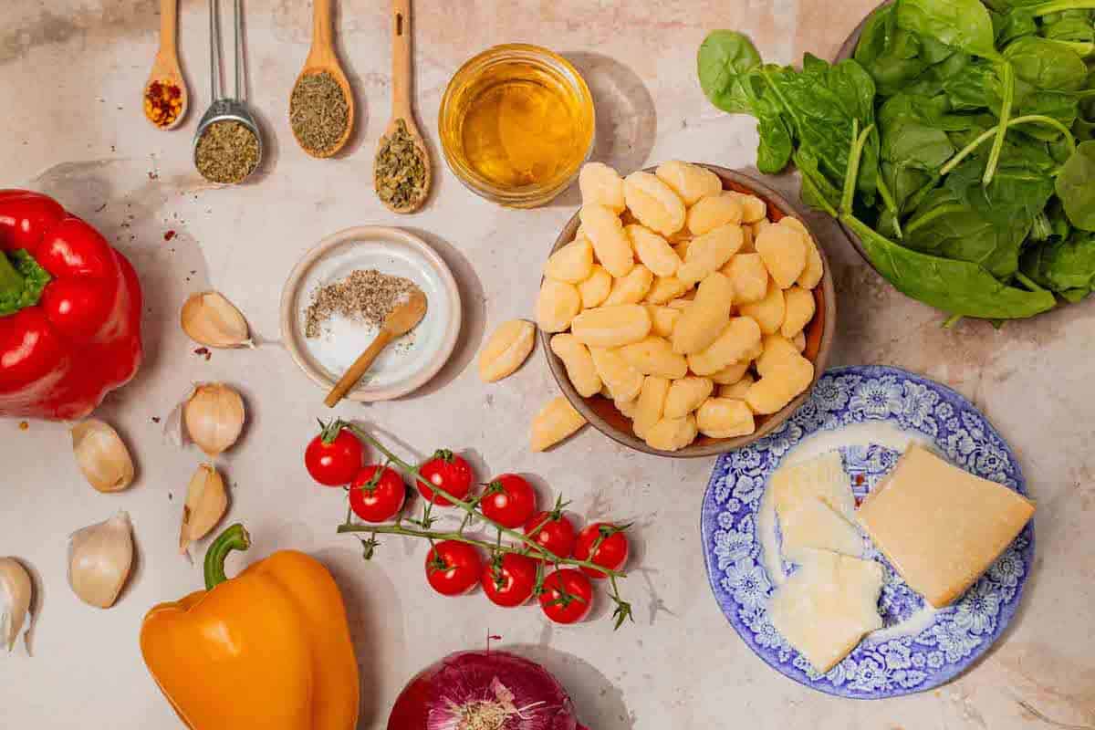 Ingredients for sheet pan gnocchi, including cherry tomatoes, parmesan cheese, gnocchi, spinach, red onion, red and yellow bell pepper, garlic, salt, dried thyme, red pepper flakes, dried basil, dried oregano, kosher salt, and extra virgin olive oil.