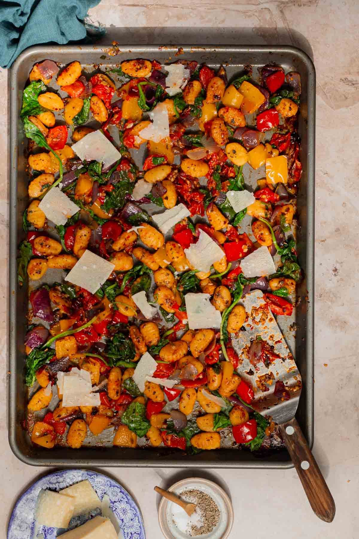 Cooked sheet pan gnocchi still in the pan with parmesan shavings on top.