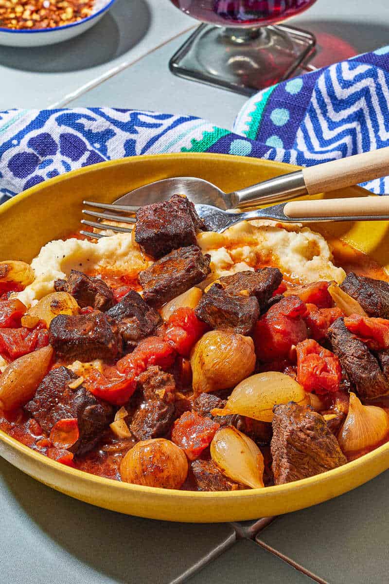 side shot of a bowl of greek beef stew on top of mashed potatoes.