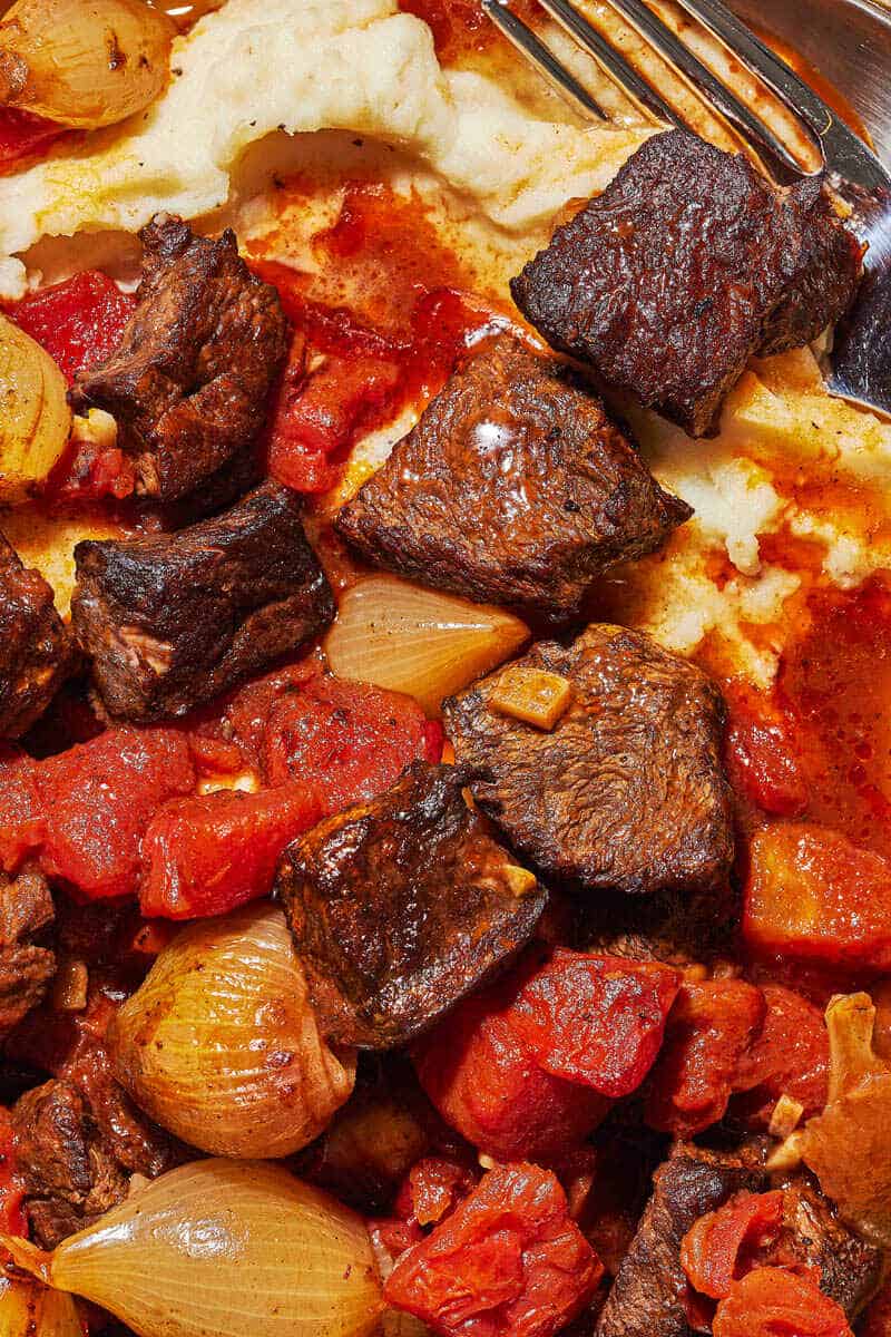 close up shot of greek beef stew, showing the nicely seared beef, tomato pieces, and pearl onions.