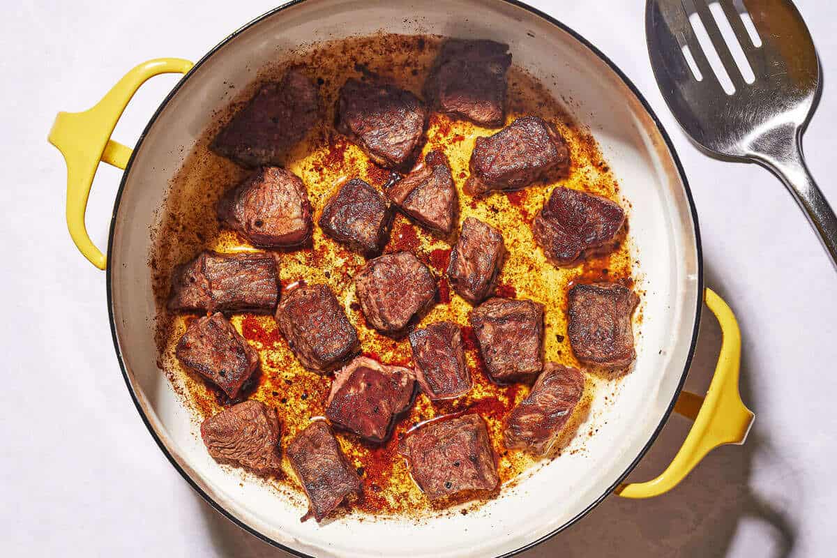 beef that has been seared in a pot with oil, showing a dark brown crust on the beef and flavorful fond sticking to the bottom of the pot.