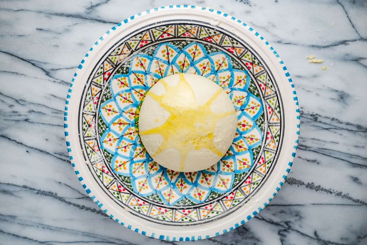 a smooth ball of mlewi flatbread dough topped with olive oil in a bowl.