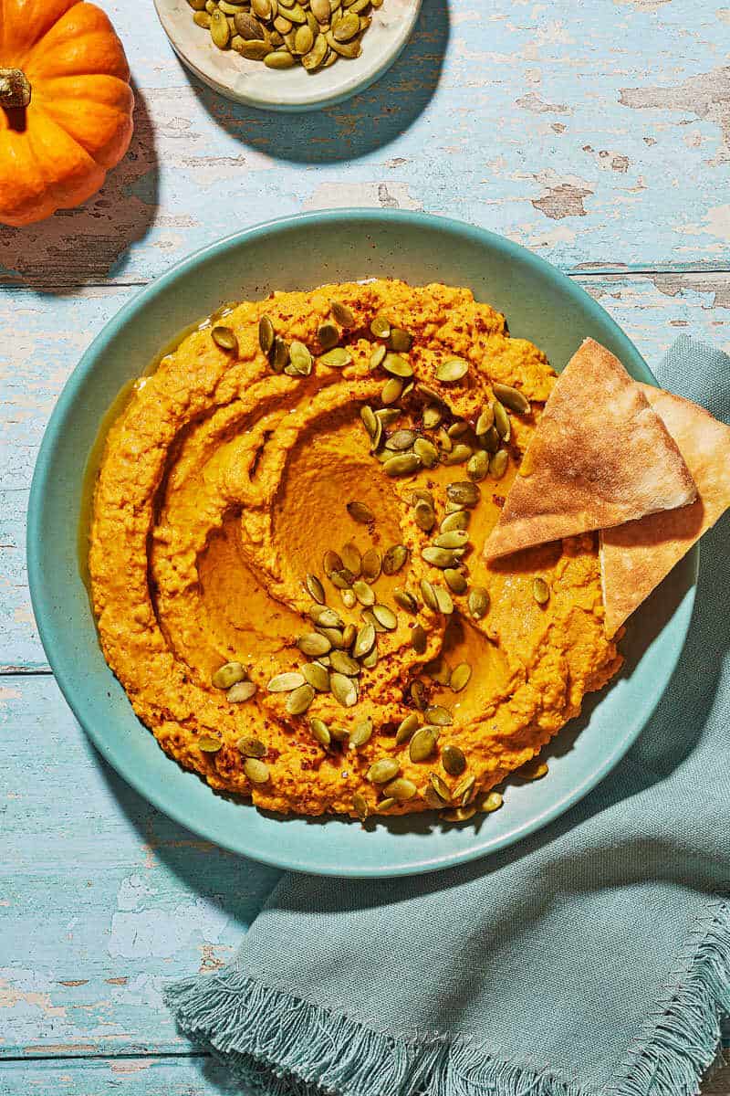 Overhead shot of pumpkin hummus with toasted pepitas and two pieces of pita bread on top.