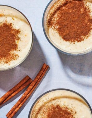 Overhead shot of four cups of Rizogalo with an orange and cinnamon sticks.