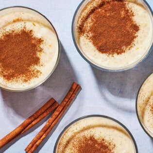 Overhead shot of four cups of Rizogalo with an orange and cinnamon sticks.