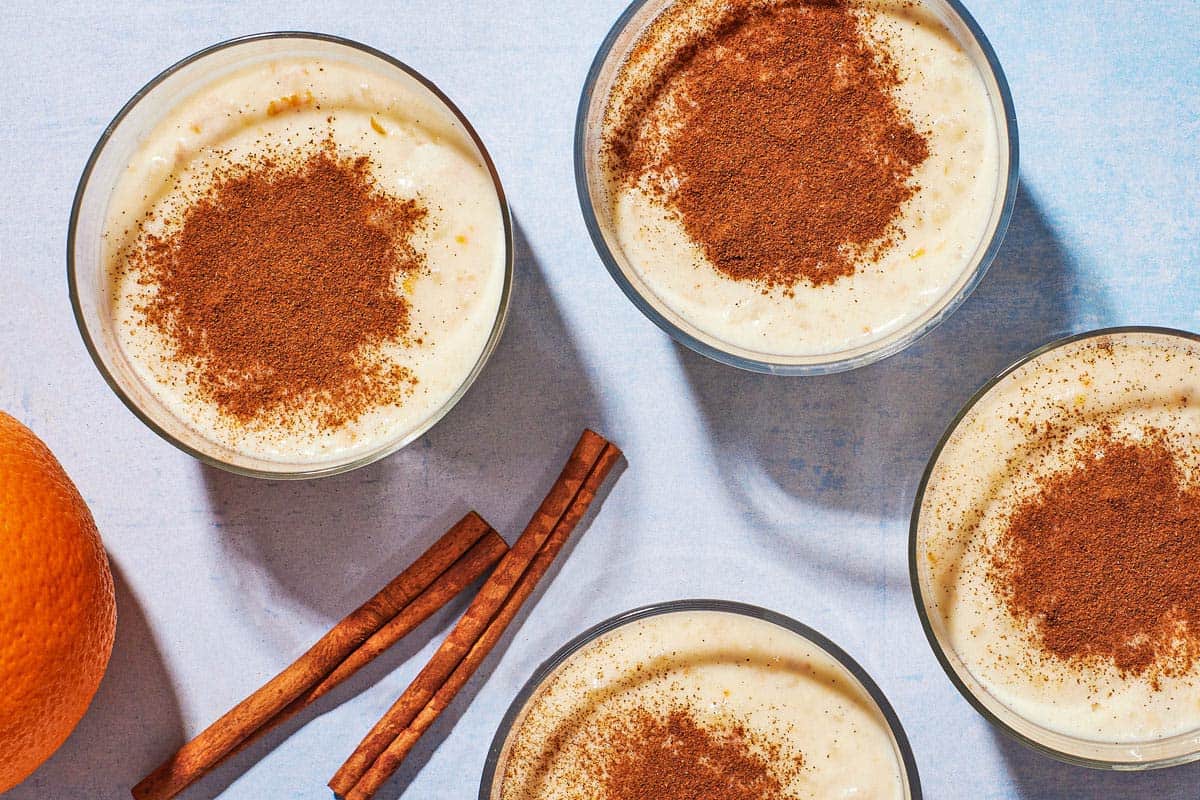 Overhead shot of four cups of Rizogalo with an orange and cinnamon sticks.