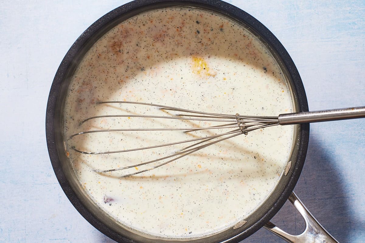 A pot whisking Rizogalo with cinnamon, milk, cinnamon stick, lemon rind, vanilla bean, and orange zest.