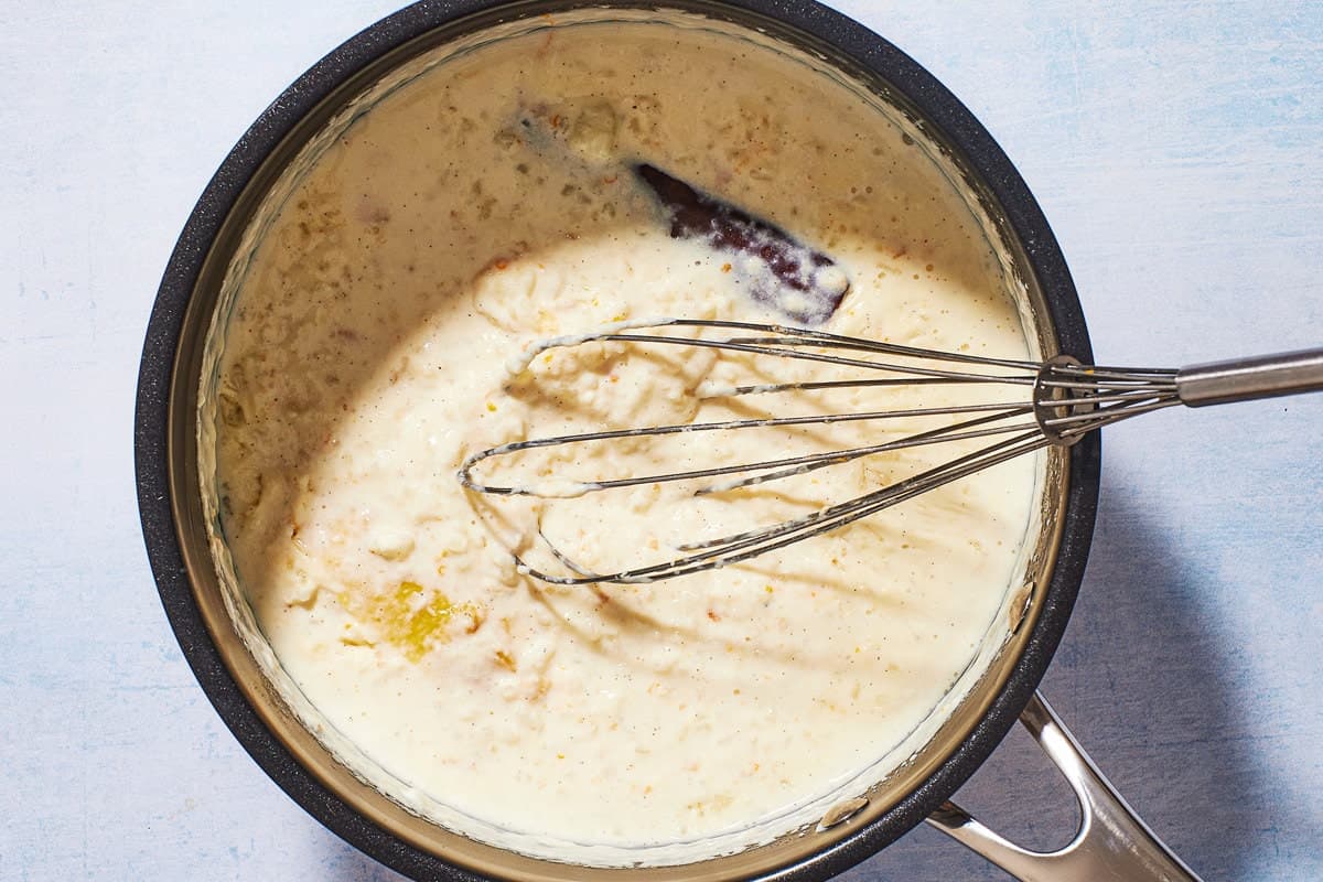 A whisk in a pot of Rizogalo after it has cooked, showing the thickened consistancy and plump rice.