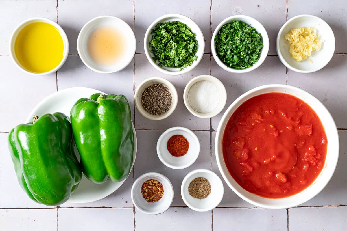 Ingredients for taktouka, including green bell peppers, canned tomatoes, red pepper flakes, salt, pepper, garlic, paprika, coriander, parsley, cilantro, olive oil, and red wine vinegar.