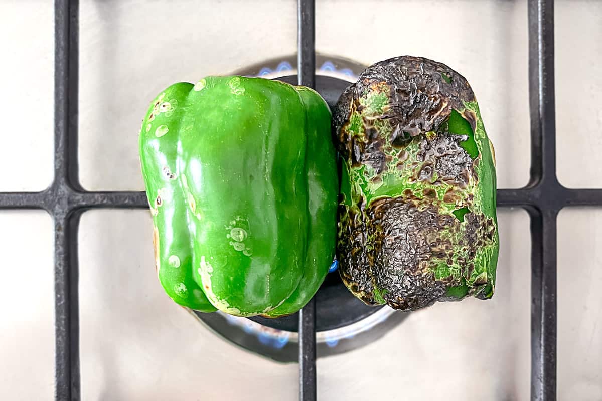 two green bell peppers roasting on a stove top, showing the charred skin.