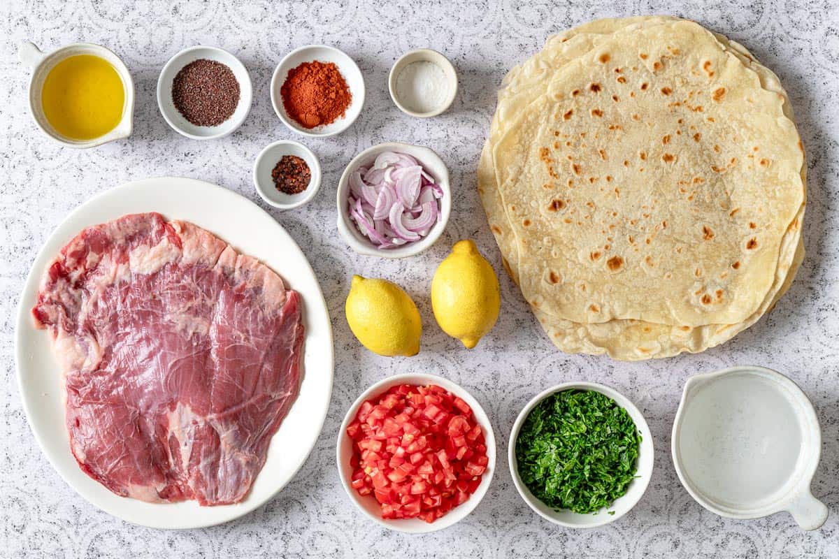 ingredients for tantuni, including lemon, steak, lavash bread, aleppo pepper, sumac, paprika, salt, steak, parsley, tomatoes, water, and olive oil.