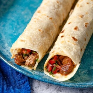 close up shot of the top of two tantuni steak wraps, showing the steak and tomato salad.