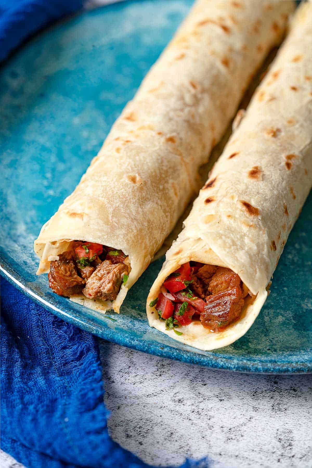 close up shot of the top of two tantuni steak wraps, showing the steak and tomato salad.