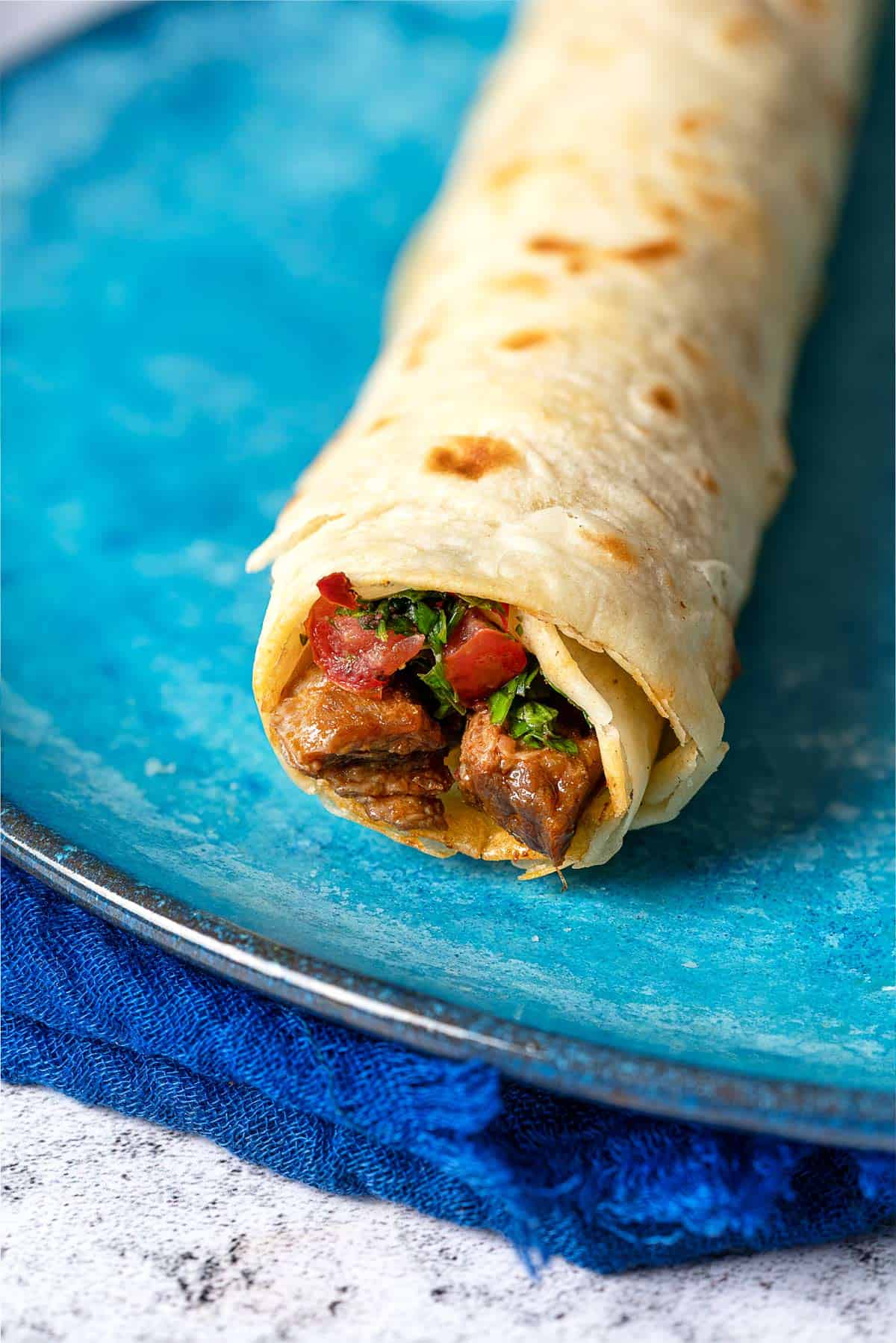 Close of shot of a tantuni steak wrap that has been filled with steak and tomato salad.