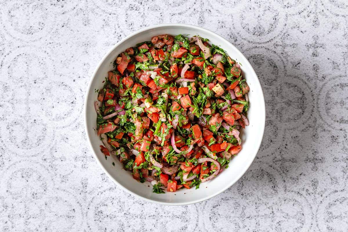 tomatoes, onion, parsley, sumac, and aleppo pepper tossed together in a white bowl.