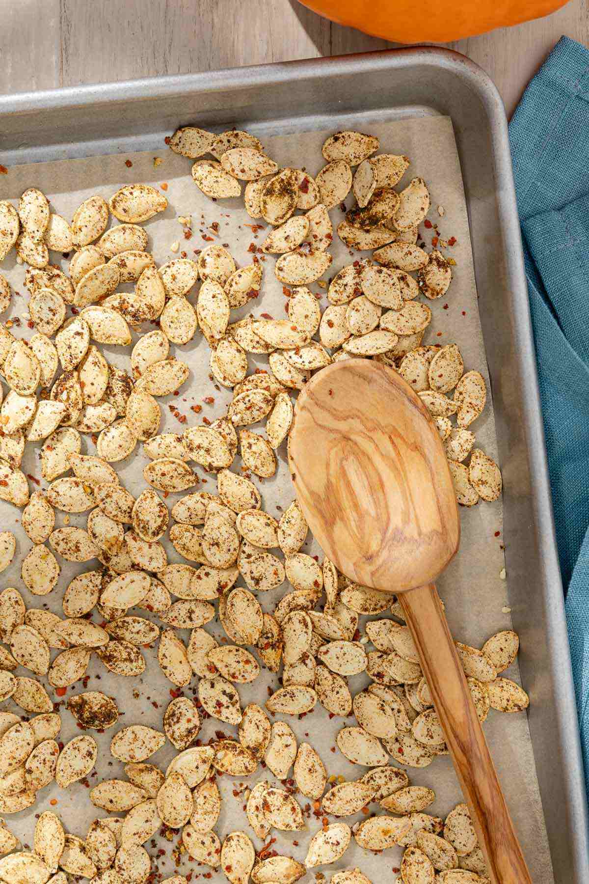 a roasted pumpkin seed recipe where there is a close-up of savory seasoned roast pumpkin seeds with a wooden serving spoon on a parchment-lined sheet pan.