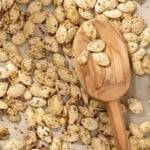 a close up of savory seasoned roast pumpkin seeds with a wooden serving spoon on a parchment lined sheet pan.