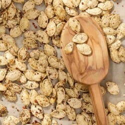 a close up of savory seasoned roast pumpkin seeds with a wooden serving spoon on a parchment lined sheet pan.