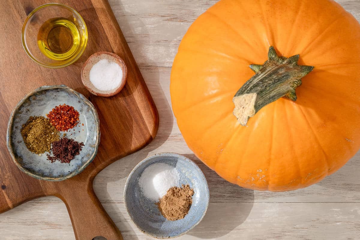 ingredients for a roasted pumpkin seed recipe including a pumpkin, olive oil, kosher salt, cinnamon, sugar, za'atar, sumac, and Aleppo pepper.