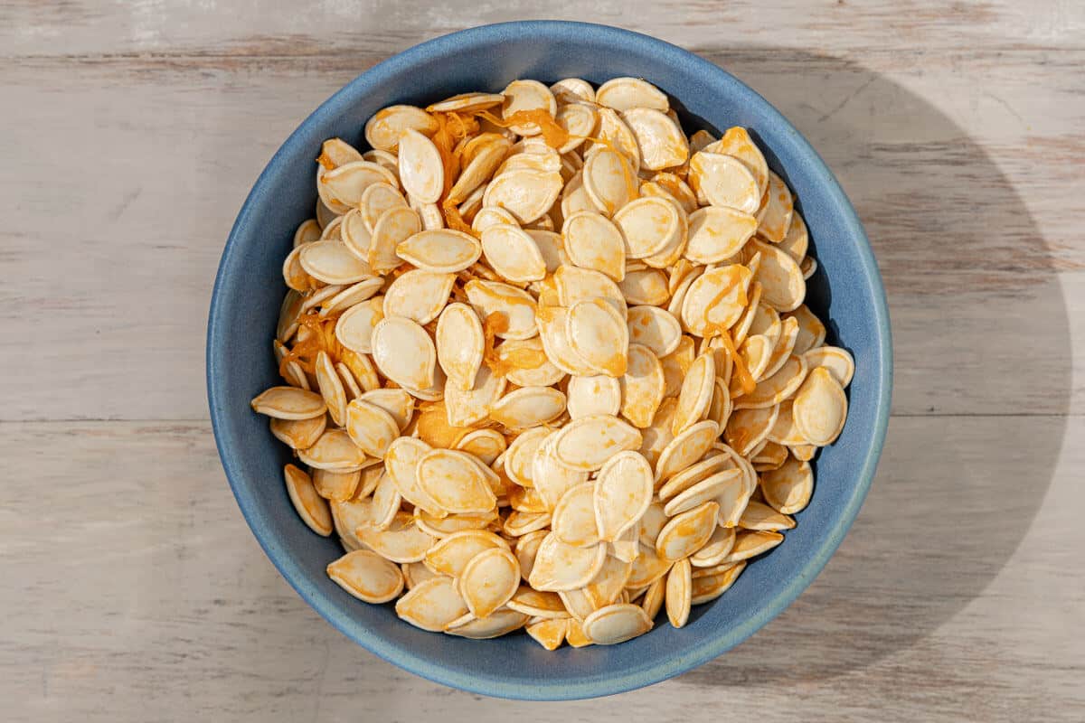 an overhead photo of raw pumpkin seeds in a bowl.