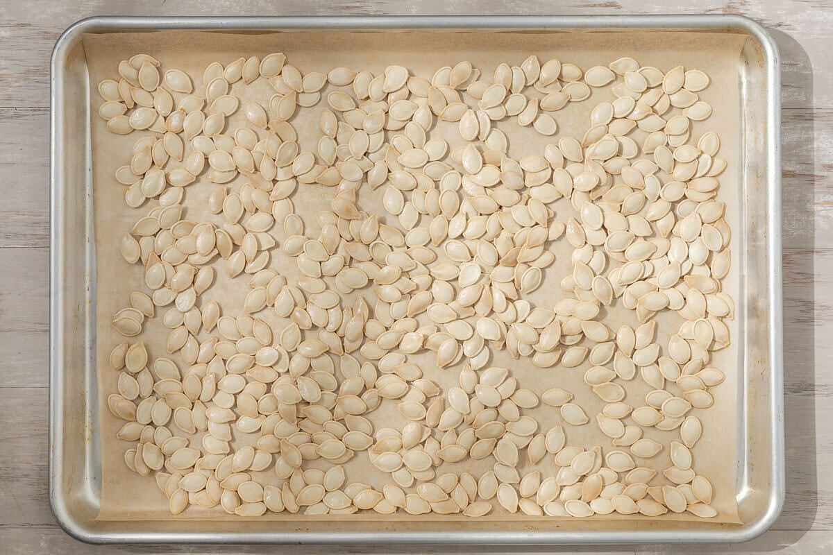 raw pumpkin seeds spread on a parchment lined sheet pan.
