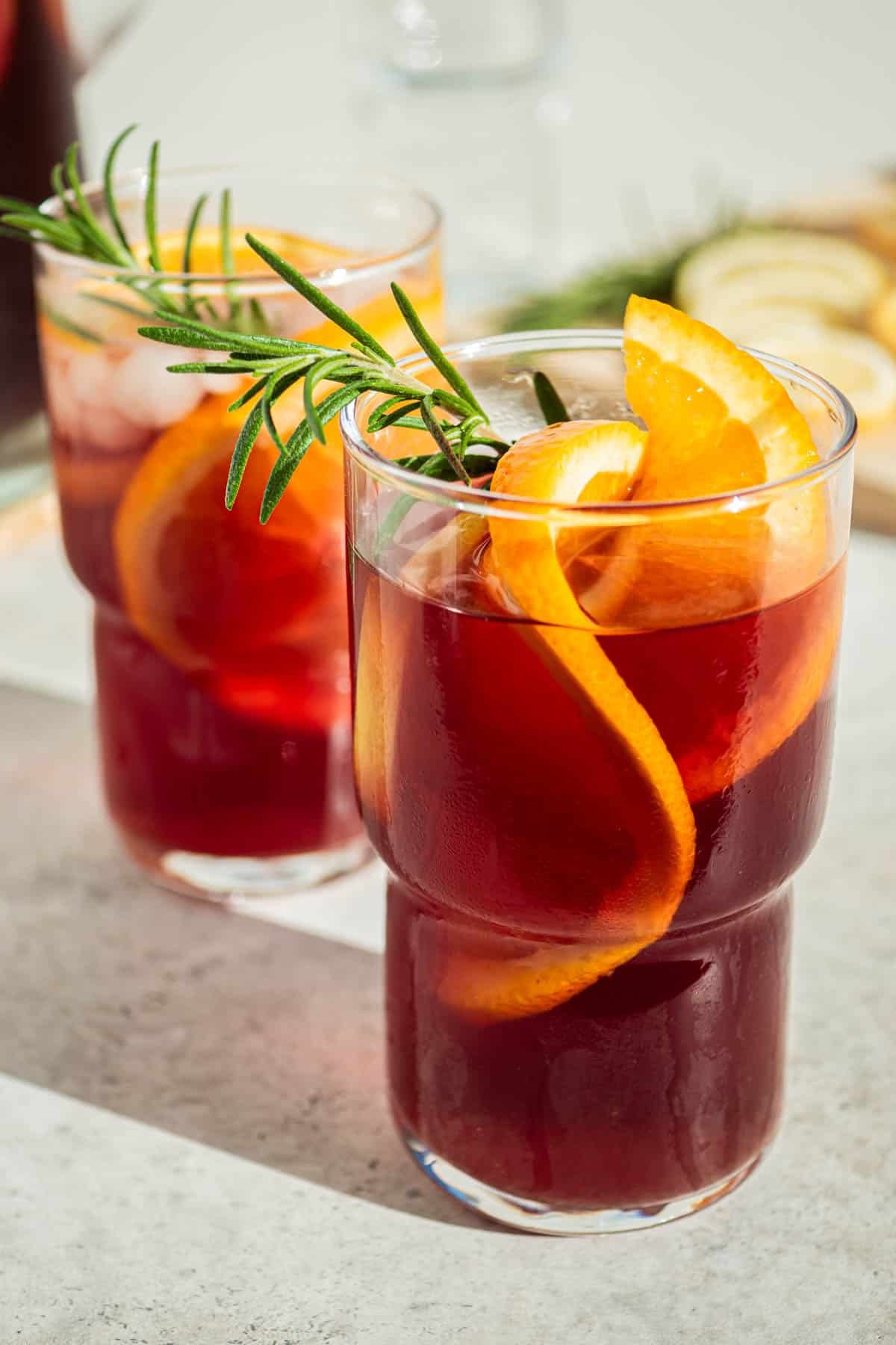 two glasses of holiday sangria garnished with orange wheels and sprigs of rosemary.