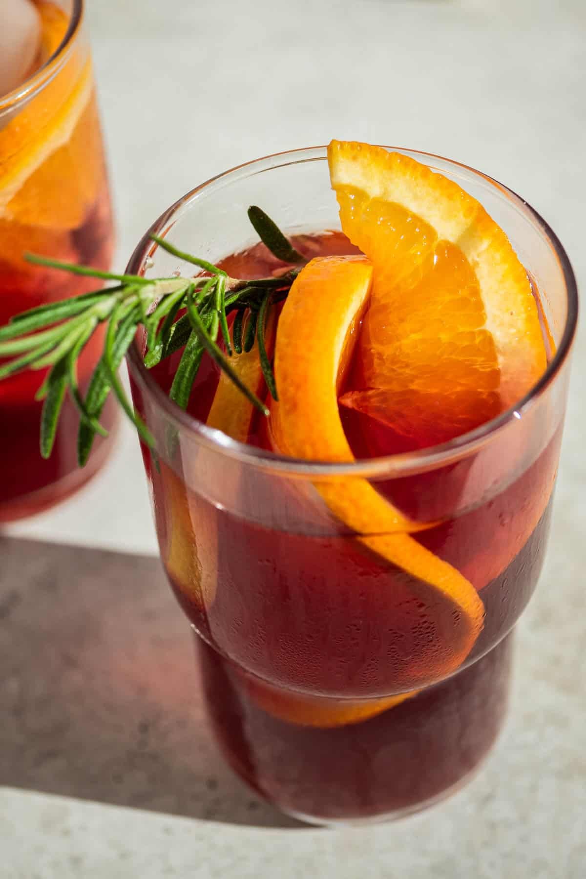 a close up of a glass of holiday sangria garnished with orange wheels and a sprig of rosemary.