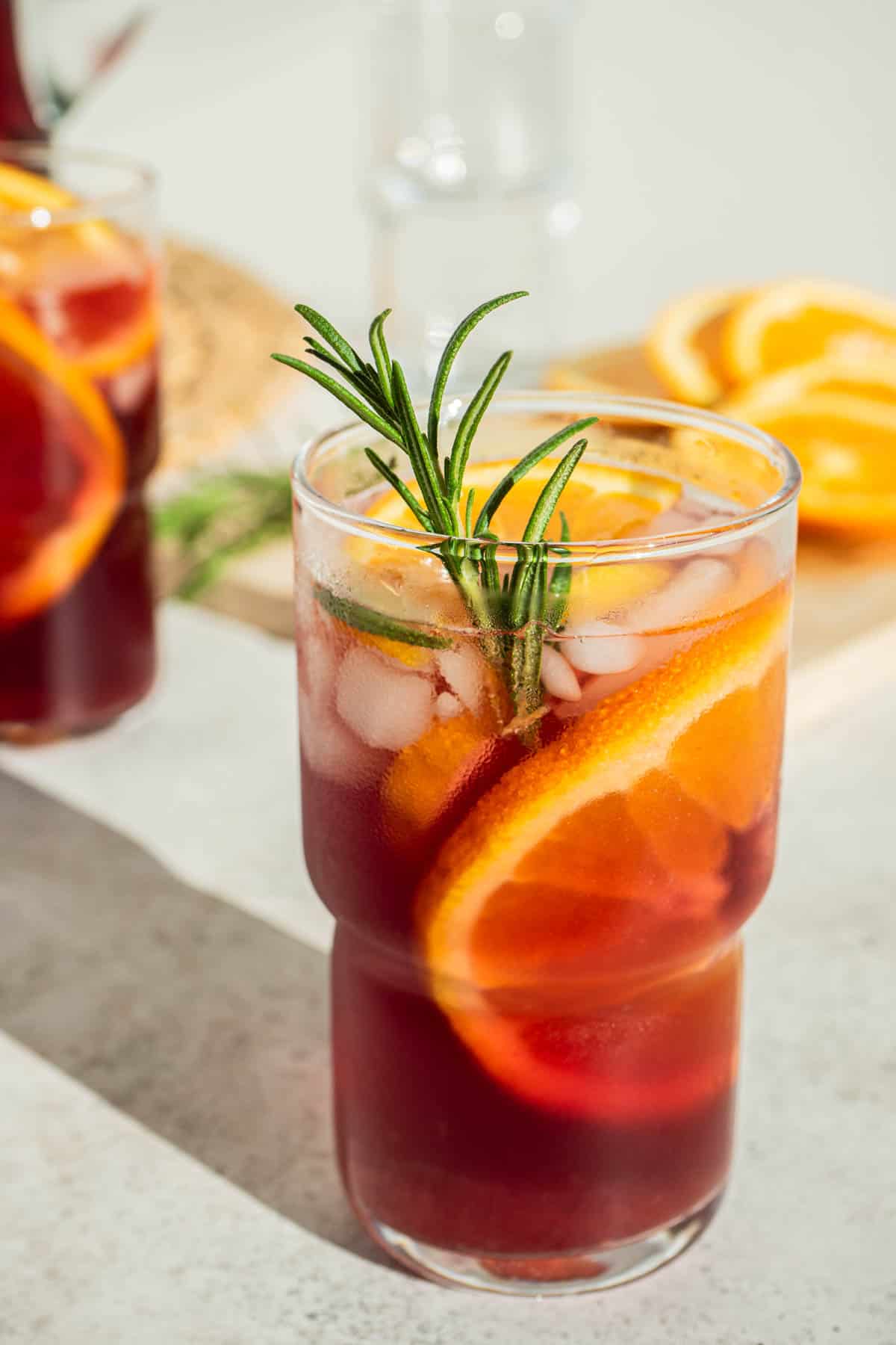 a glass of holiday sangria garnished with orange wheels and a sprig of rosemary.