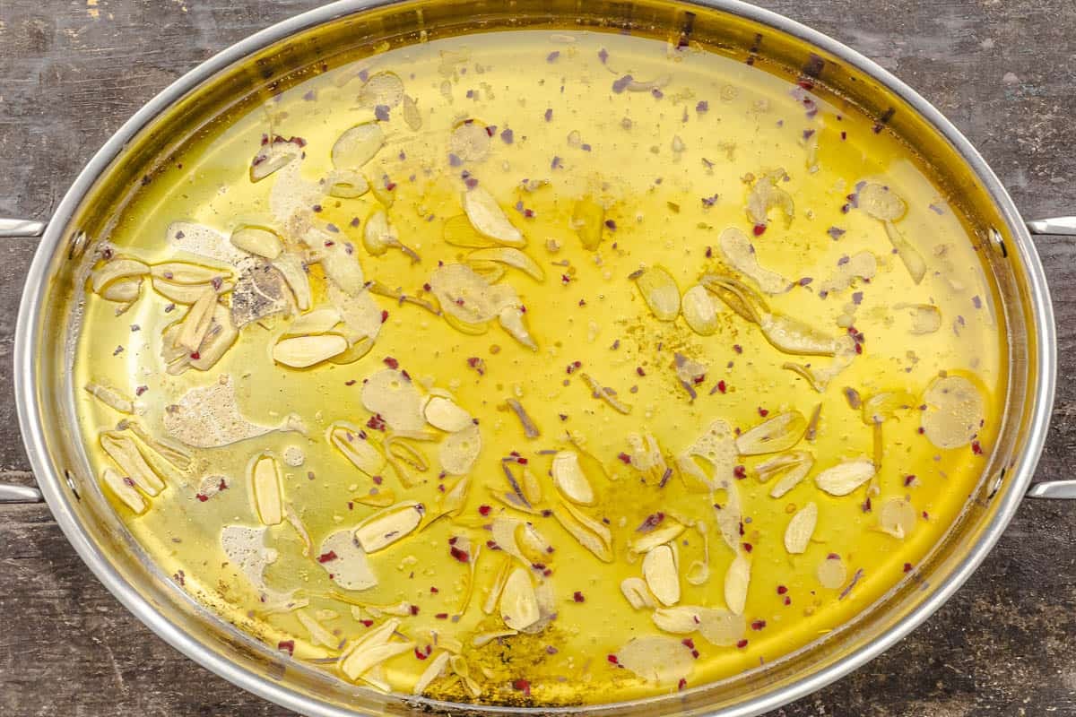 garlic and red pepper flakes cooking in olive oil in a stainless steel pan.