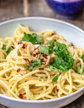 a close up of spaghetti aglio e olio topped with grated parmesan, red pepper flakes and parsley in a bowl.