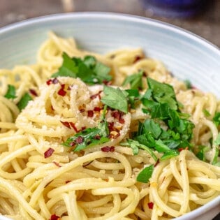 a close up of spaghetti aglio e olio topped with grated parmesan, red pepper flakes and parsley in a bowl.