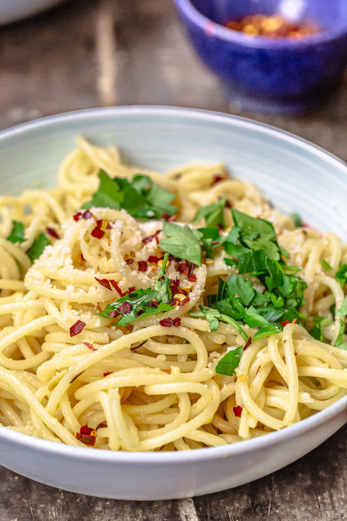 a close up of spaghetti aglio e olio topped with grated parmesan, red pepper flakes and parsley in a bowl.