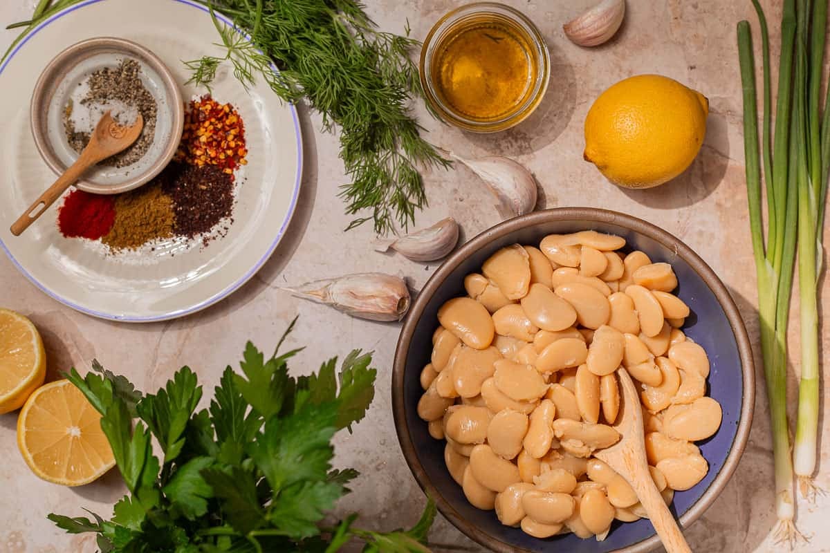 Ingredients for butter beans, including olive oil, red pepper flakes, Urfa pepper, cumin, paprika, garlic, salt, pepper, butter beans, broth, lemons, green onions, parsley, and dill.