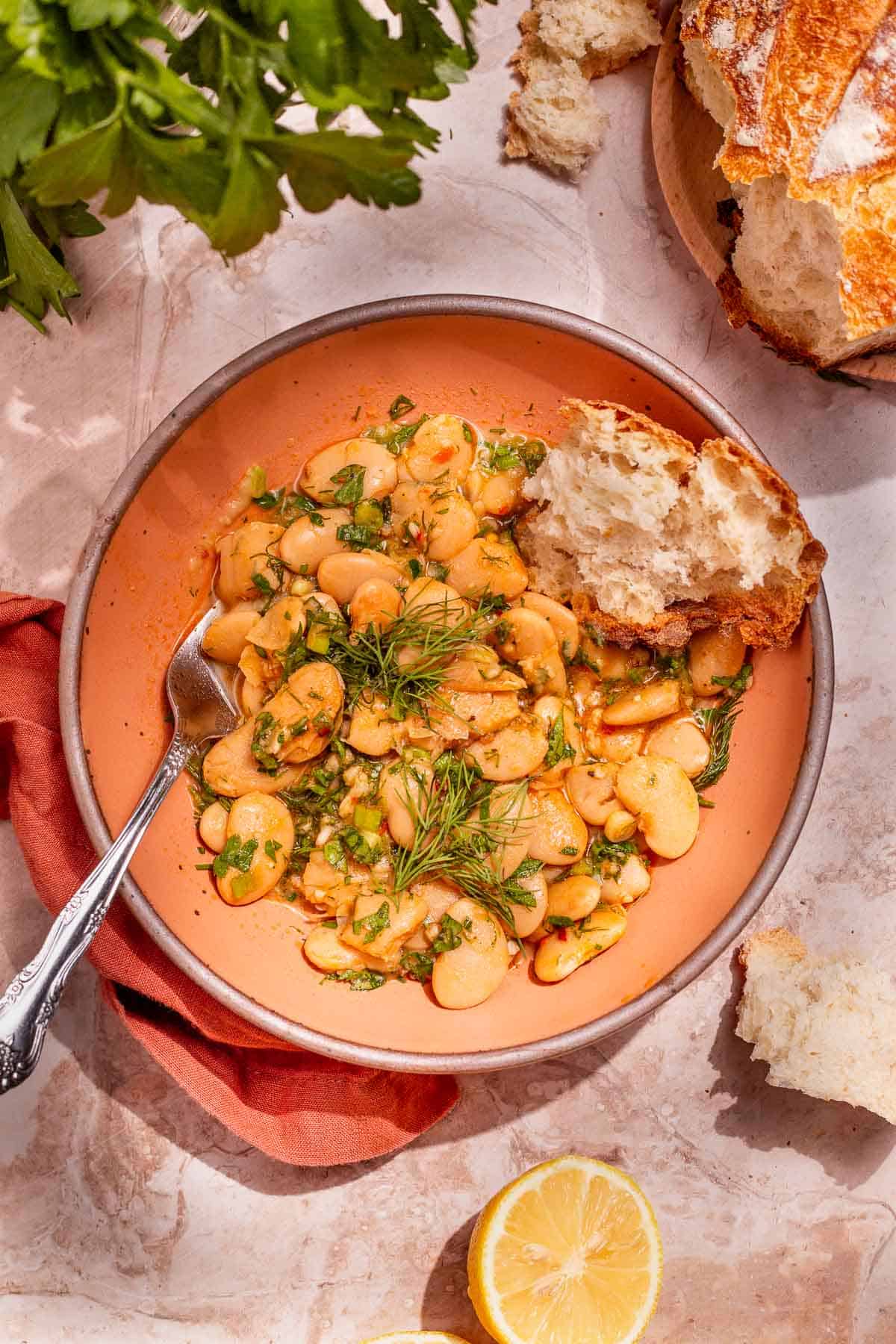 Overhead shot of butter beans in a peach-colored bowl with a silver fork and a torn piece of crusty bread.