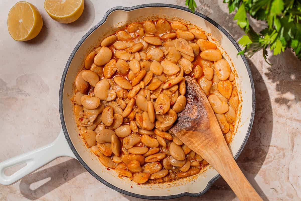 Beans coated in spiced oil in a white skillet.