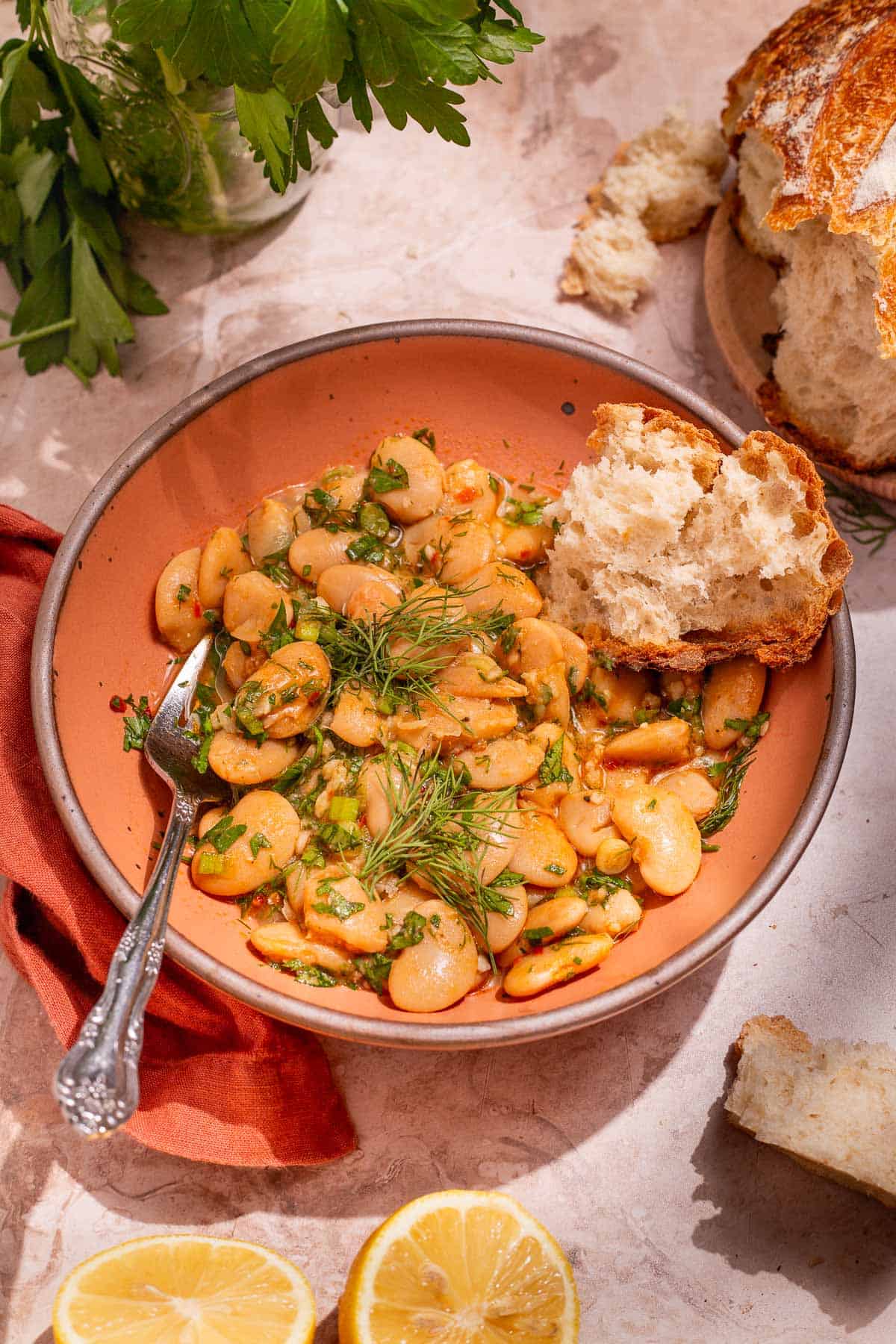 Serving of butter beans in a peach-colored bowl with a silver fork and a torn piece of crusty bread.