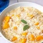 a close up of one bowl of butternut squash risotto topped with parmigiano-reggiano cheese sage leaves.