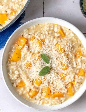 an overhead photo of a bowl of butternut squash risotto topped with parmigiano-reggiano cheese sage leaves.