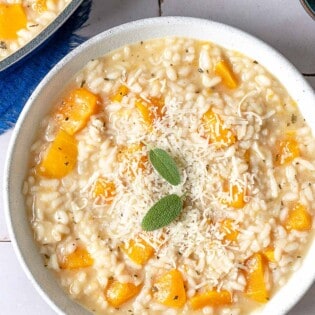 an overhead photo of a bowl of butternut squash risotto topped with parmigiano-reggiano cheese sage leaves.