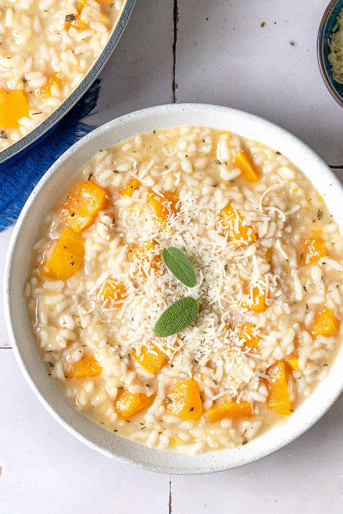 an overhead photo of a bowl of butternut squash risotto topped with parmigiano-reggiano cheese sage leaves.
