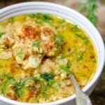 a close up of roasted cauliflower soup in a bowl with a spoon garnished with dill.