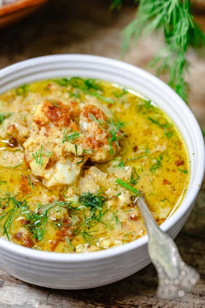 a close up of roasted cauliflower soup in a bowl with a spoon garnished with dill.