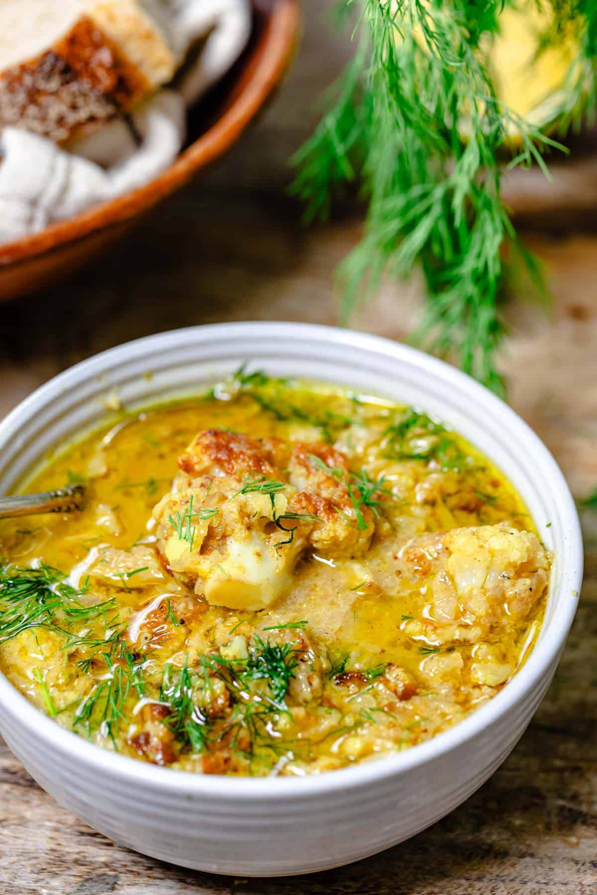 a close up of roasted cauliflower soup in a bowl with a spoon garnished with dill.