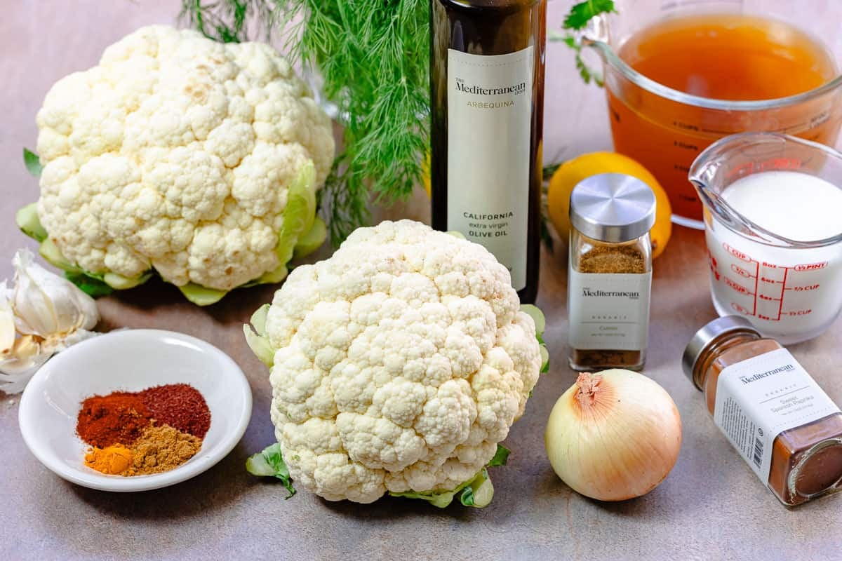 ingredients for cauliflower soup including cauliflower, broth, onion, garlic, cumin, sweet paprika, sumac, turmeric, milk, lemon, olive oil and dill.