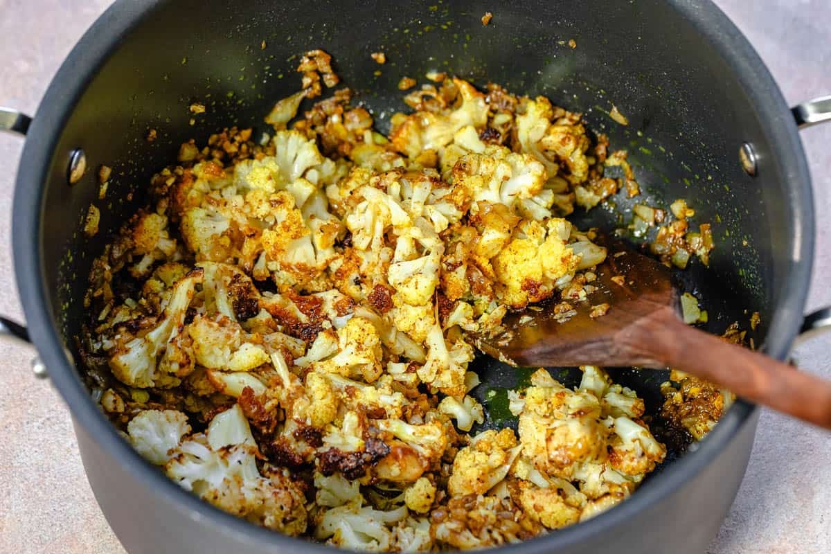 onions and roasted cauliflower being sauteed in a pot.